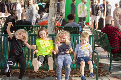 Four kids in zombie makeup make silly faces on a park bench.