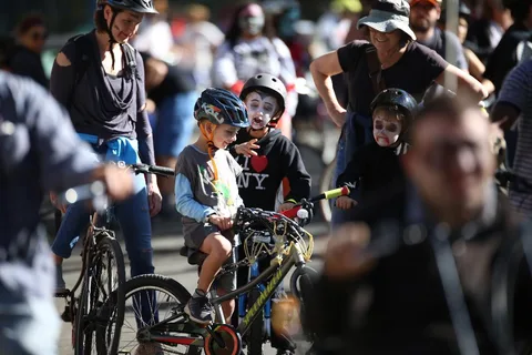 Riders in helmets gather on bikes on a tree-lined street.