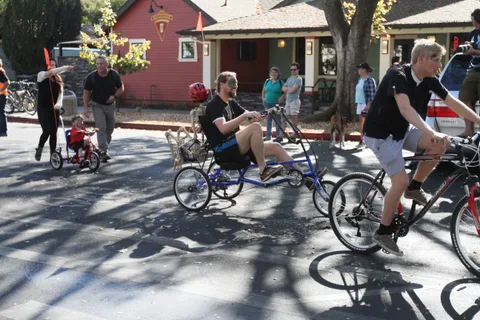 Several riders on low recumbent trikes ride together down the street.