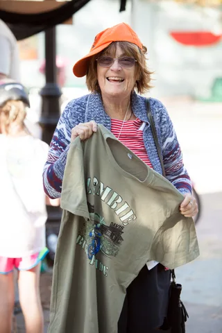 A laughing woman in an orange cap holds up an official Zombie Bike Ride Davis T-shirt.