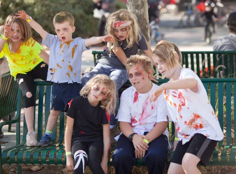 Three kids in zombie makeup sit together on a park bench.