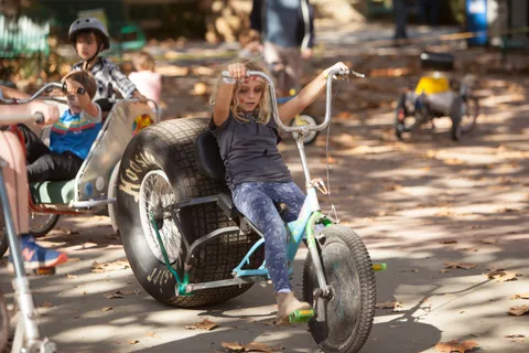 A girl throws her arms out while riding a big-wheeled chopper trike.