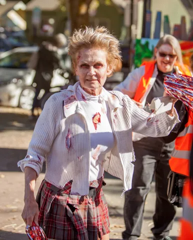 A woman in a torn, bloodied zombie cheerleader costume stares directly at the camera.