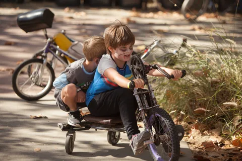 A child tumbles playfully off a small bike.