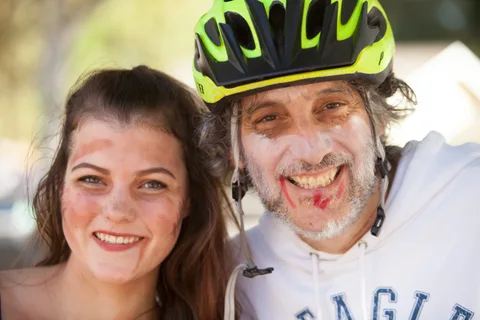 A young woman and a smiling man in a bright green bike helmet and zombie makeup pose close together.