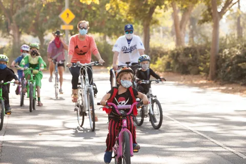 A group of costumed riders, several of them kids, ride together down the path.