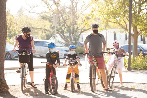A masked family stands with bikes in a parking lot.