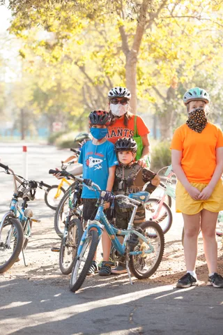 Kids stand with their bikes near a bike rack.