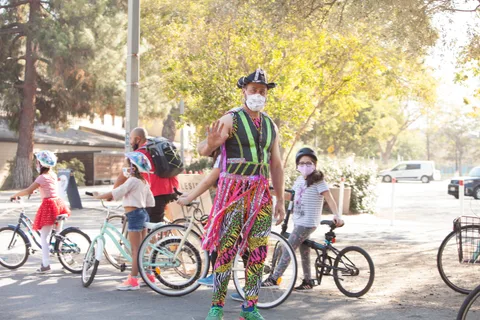 A rider in neon patterned pants stands with bikes and kids on the path.