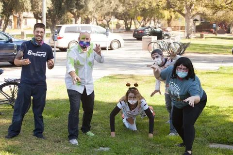 A group play-acts a zombie scene on the grass, one crouched low with arms out.