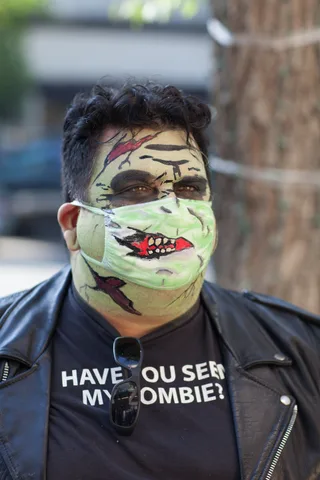A man wears a green mask painted with a zombie mouth and stitched wound.