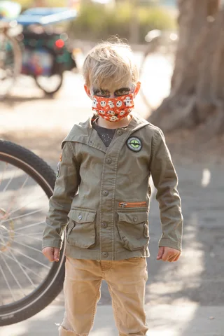 A boy in a green jacket wears a skull-print mask.