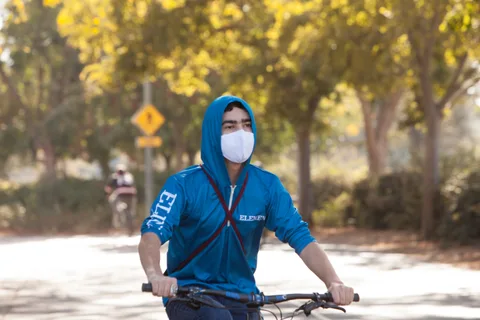 A man in a blue hoodie and mask rides alone down the path.