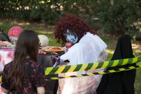 Two women in elaborate zombie makeup and costume stand near a Beware Zombies caution tape display.