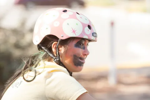A woman in a polka-dot helmet has blue face paint along her jaw in profile.