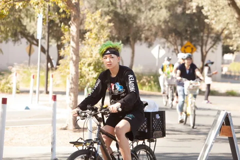 A rider in a green headband jersey pedals ahead of a line of other cyclists.