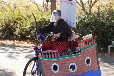 A rider in a pirate costume pedals a bike built into a full handmade cardboard pirate ship.