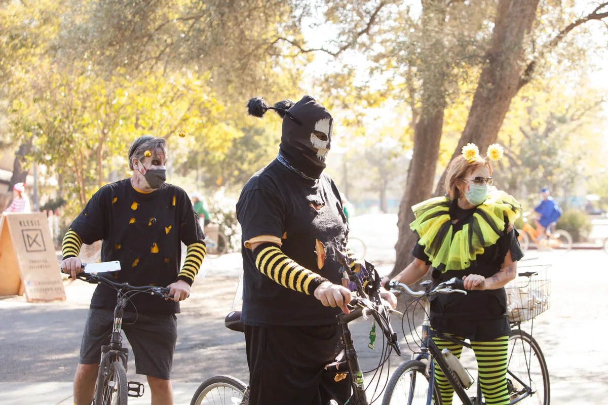 Three riders in black and yellow striped bee costumes with zombie face paint stand with their bikes
