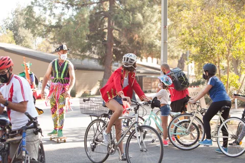 A rider in neon patterned pants and a woman in a red poncho gather with other cyclists.