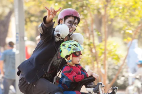 A man throws a hand sign while holding a small child among a group of masked kids in helmets.