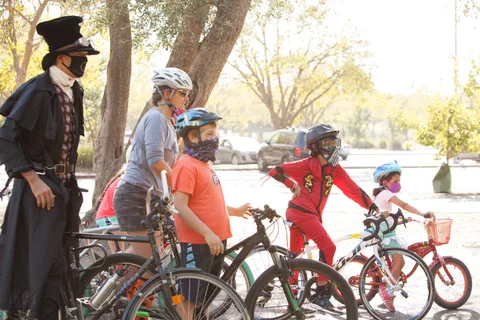 A group of costumed riders in orange and red stand together with their bikes.