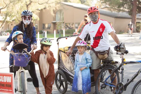 A child in a bear costume stands with family members and bikes near a jersey-wearing man.