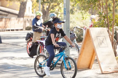 Two riders pass a wooden A-frame route sign on the path.