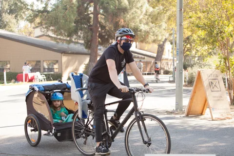 A man rides a bike pulling a child trailer through the park.
