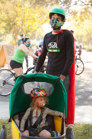 A rider in a tropical shirt and red mask stands with a green cargo trailer bike.
