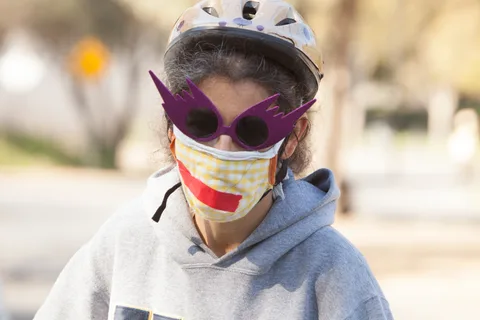 A woman in purple sunglasses wears a mask painted with a fanged mouth.