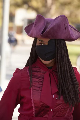 A close detail of a purple tricorn pirate hat over braided hair and a mask.