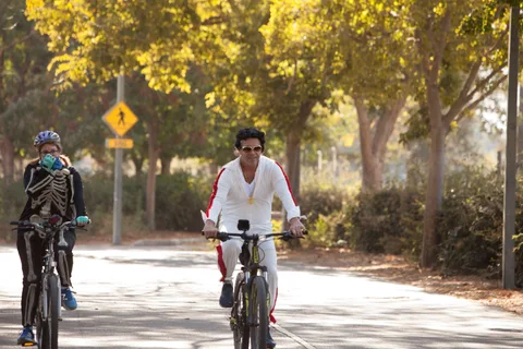 A man in a white skeleton-print shirt and sunglasses rides alone.