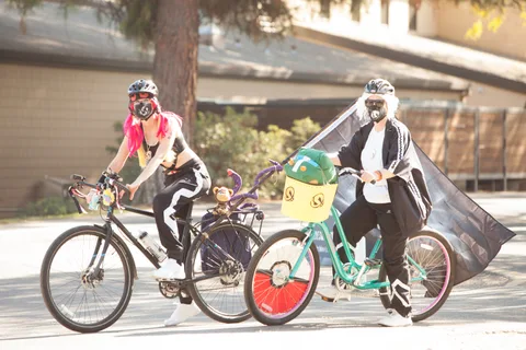 A rider in a white skeleton cape pulls a green cargo trailer along the path.