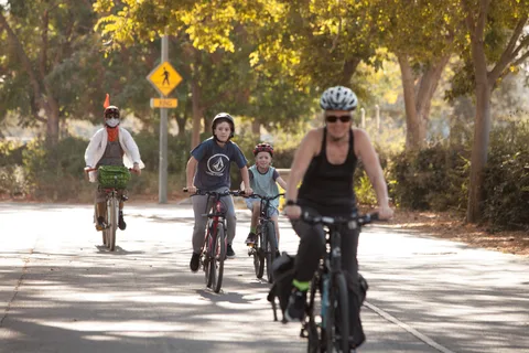A rider in a white skeleton costume waves as a kid and a small dog follow behind.