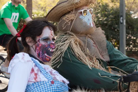 A zombie Dorothy and a bloodied scarecrow in a straw hat and sunglasses pose close together.