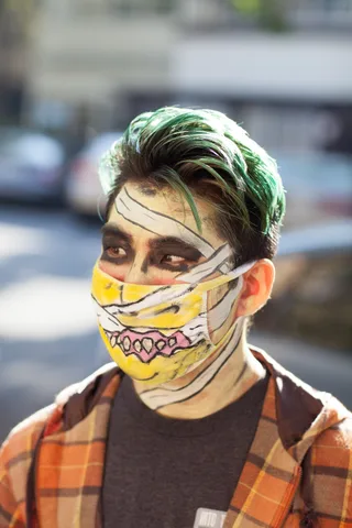 A man wears a Halloween mask painted with a cartoon mouth under a plaid flannel jacket.