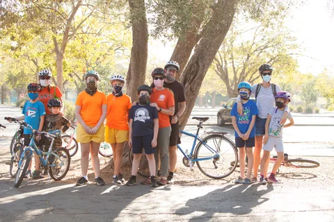 A family group with bikes and helmets poses together under the trees.