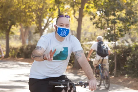 A tattooed rider in a blue mask flashes a peace sign while riding.