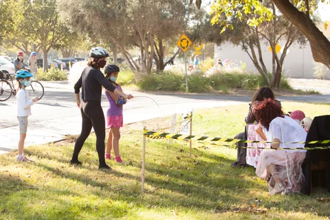 Small figures stand on the grass near a caution-tape barrier.