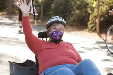 A rider on a recumbent trike waves with a colorful flag mounted behind her.