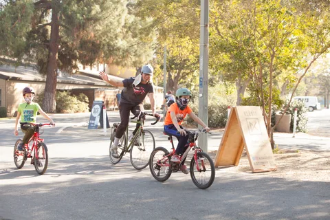 Kids ride bikes past a wooden route sign in the park.