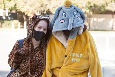 Two people in matching leopard and elephant onesie hoods pose together.