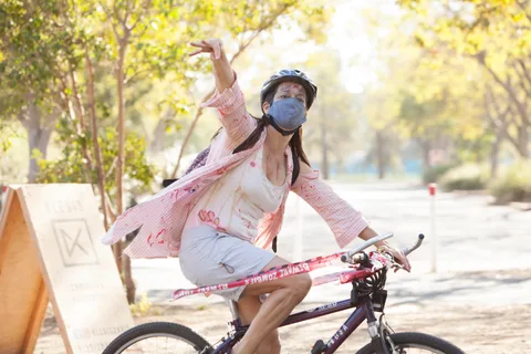 A costumed rider throws a fist in the air while pedaling past a Klesis sign in golden light.