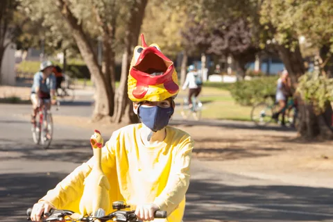 A rider in a yellow bodysuit with a dragon-headed hat rides past.