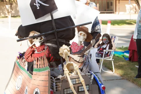 A handmade pirate ship bike float is decorated with a skeleton band and a jolly roger flag.