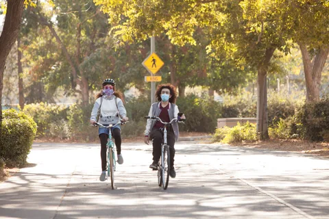 Two masked riders approach the camera past a pedestrian crossing sign.