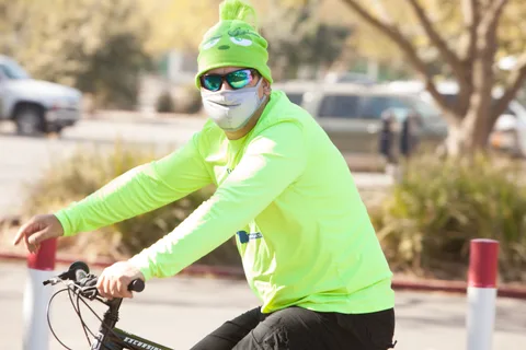 A man in a bright green shirt and beanie waves while riding.