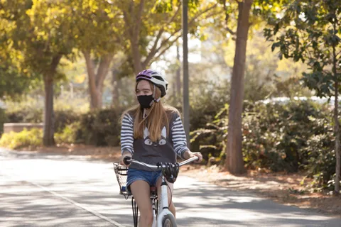 A masked rider in a striped shirt pedals down the path.