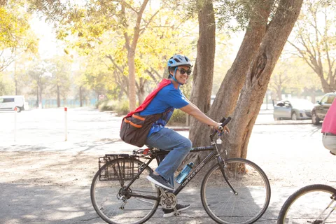 A rider in a blue cape pedals away through the park.