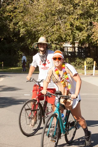 A couple in cowboy and flower-lei costumes pose with a red bike.